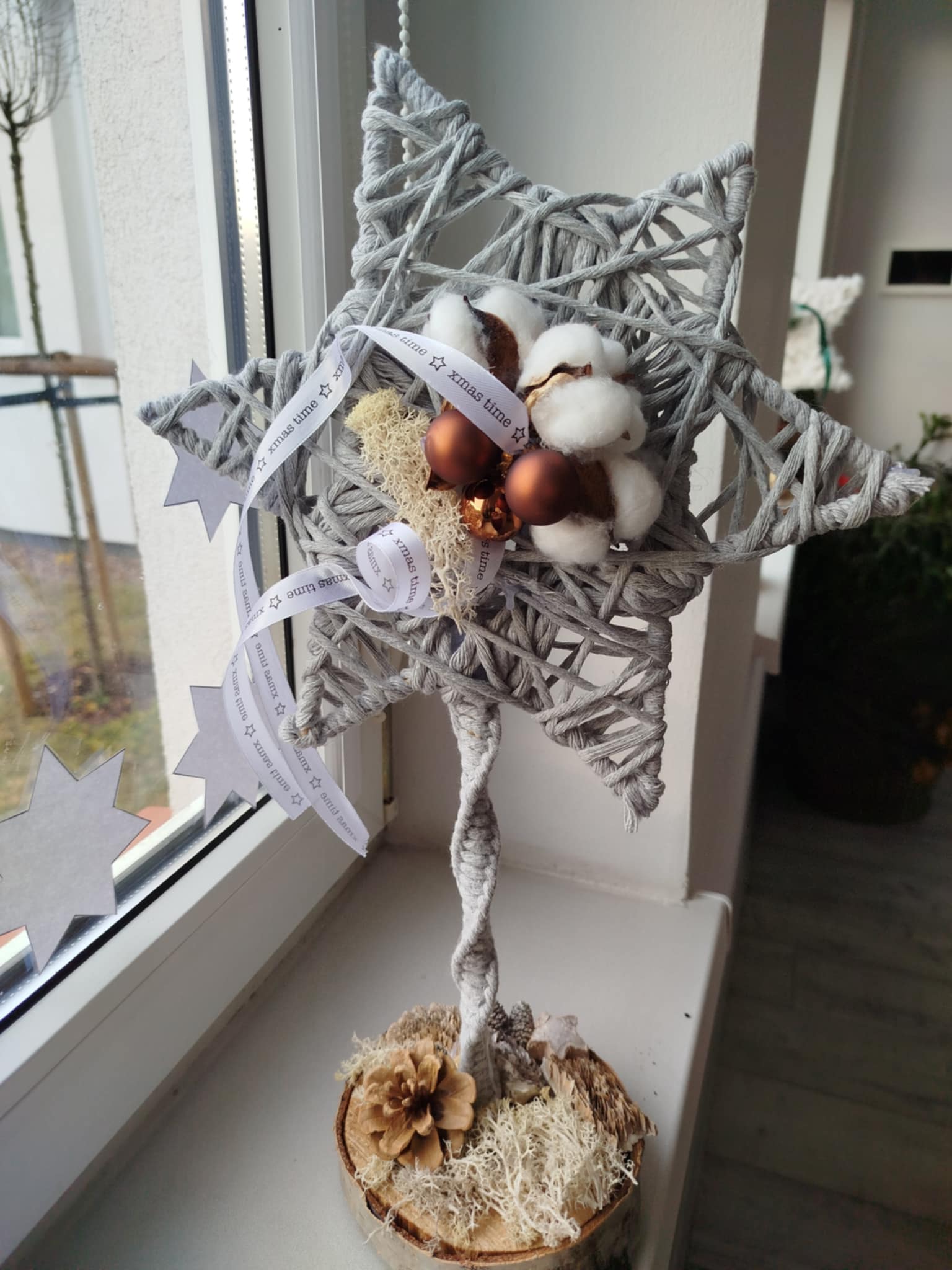 Stojący stroik zrobiony ze sznurka, udekorowany białą wstążką, kulkami bawełny i bombkami w odcieniach miedzianych
