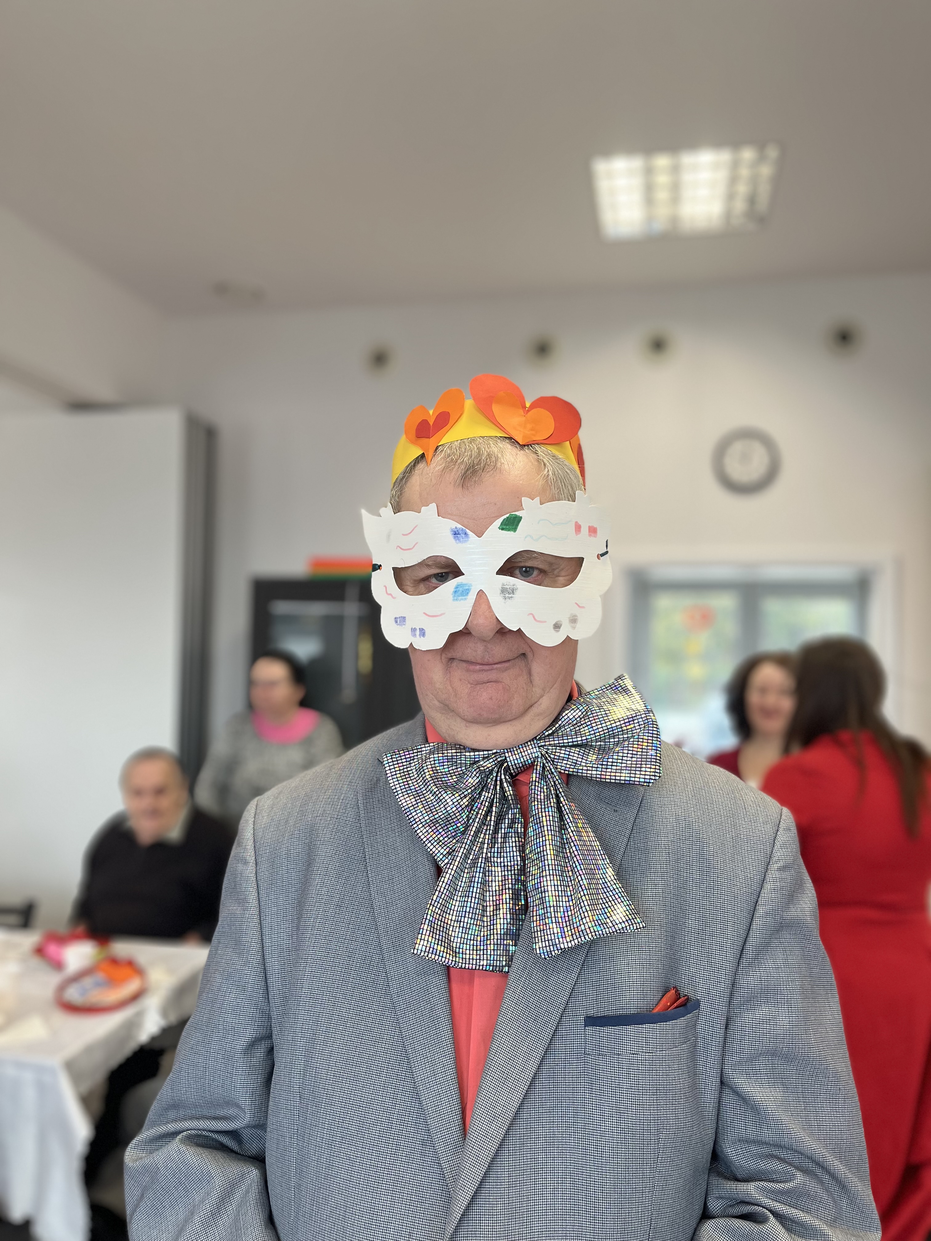 Uczestnik ŚDS w karnawałowej kreacji, w białej masce i żółtej koronie z pomarańczowo-czerwonymi sercami z papieru