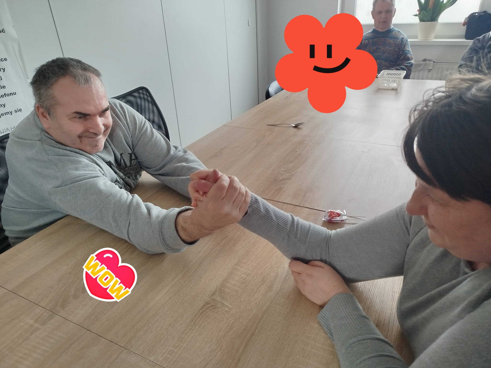 Mężczyzna i kobieta trzymają się dłońmi przy stole w pozycji jak gdyby mieli się siłować.