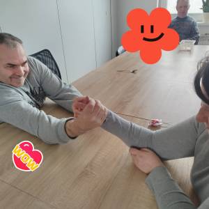 Mężczyzna i kobieta trzymają się dłońmi przy stole w pozycji jak gdyby mieli się siłować.