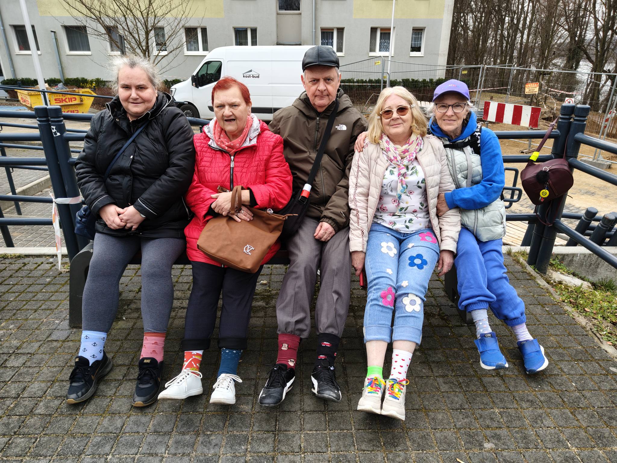 Pięć osób siedzących na ławce pozuje do zdjęcia z podwiniętymi nogawkami, pokazując kolorowe skarpetki