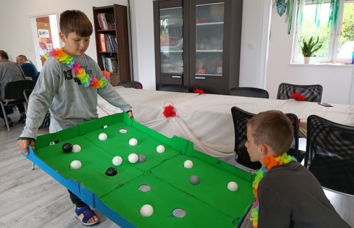 Dwóch chłopców trzyma kartonową planszę przypominającą stół bilardowy, z białymi i czarnymi kulami.