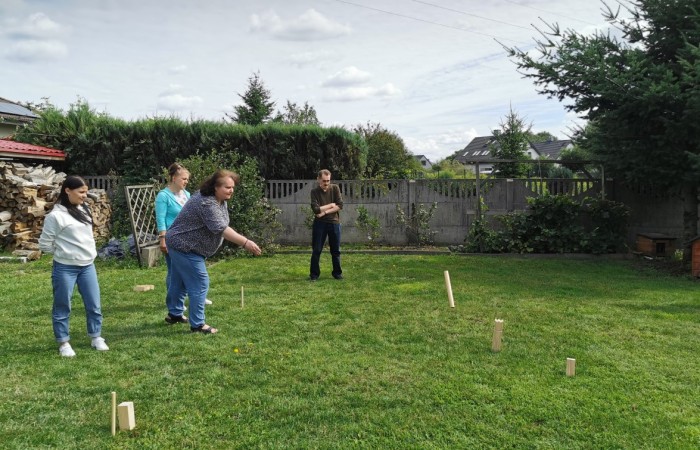 Grupa osób gra w grę na świeżym powietrzu, w ziemi powbijane są drewniane kołki