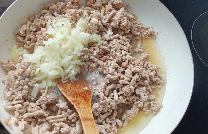 Mięso i cebula smażone na patelni i mieszane drewnianą łyżką 