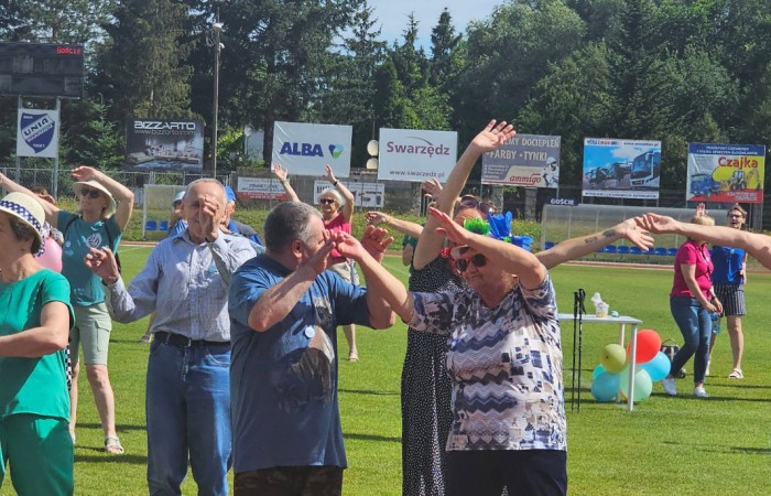 Seniorzy podnoszą ręce podczas aktywności ruchowej na boisku.
